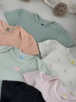 نمای نزدیک بادی نوزادی دخترانه H&M با سرشانه چیندار در رنگ‌های پاستلی سبز سدری، هلویی و صورتی با طرح گیلاس