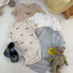 ست کامل بادی آستین کوتاه نوزادی H&M در رنگ‌های خنثی با طرح سگ داشوند همراه با کلاه حصیری، عروسک خرس و کفش نوزادی