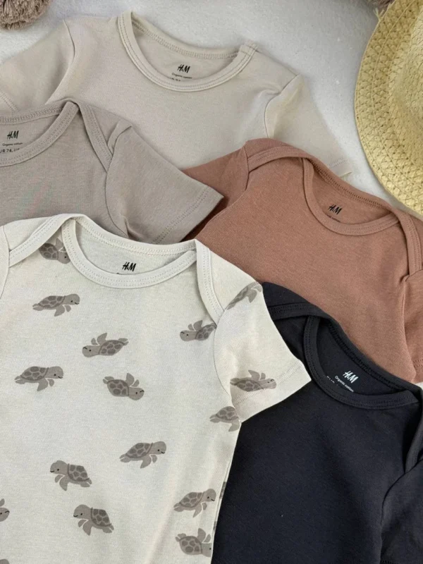 نمای نزدیک لوگوی اورجینال H&M و برچسب پنبه ارگانیک روی یقه بادی نوزادی در رنگ‌های خاکی با طرح لاک‌پشت